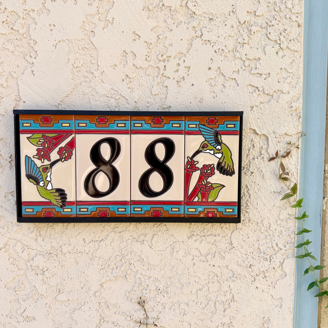 Decorative house number sign with birds on a textured wall.