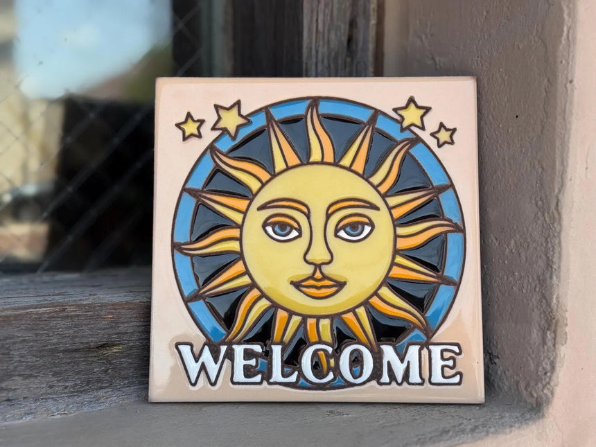 Decorative tile with sun and moon design and 'WELCOME' text on a wooden surface.